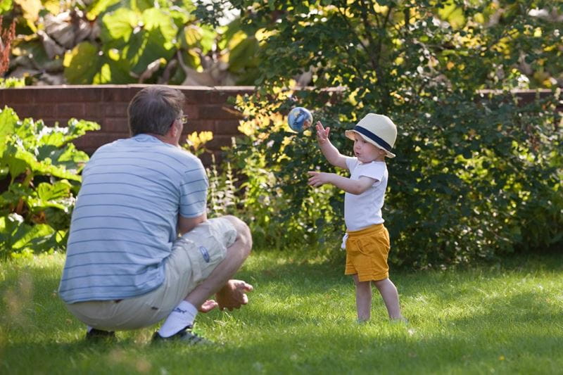Mies ja pikkupoika pelaavat palloa pihalla